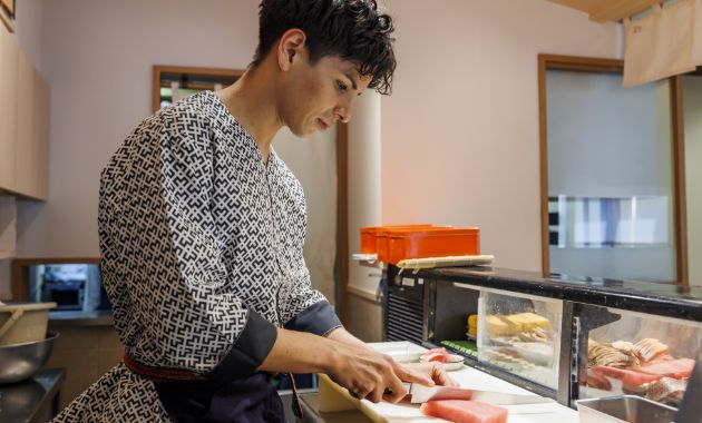 キッチンで寿司ネタの魚を切っているスタッフの写真